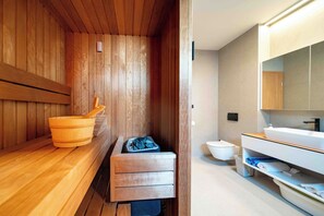 A sauna with wooden walls and a wooden bench. There is a wooden bucket and a towel rack. A white sink and a mirror are visible in the adjacent bathroom. - 5 stars Luxury Villa in Lopar on island Rab (LOPAR (RAB))
