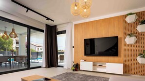 A modern living room with a large flat-screen TV, wooden panel wall, and a dining area with outdoor view. - 5 stars Luxury Villa in Lopar on island Rab (LOPAR (RAB))