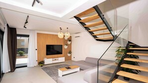 A modern living room with a glass staircase, a large TV, and a wooden accent wall. - 5 stars Luxury Villa in Lopar on island Rab (LOPAR (RAB))