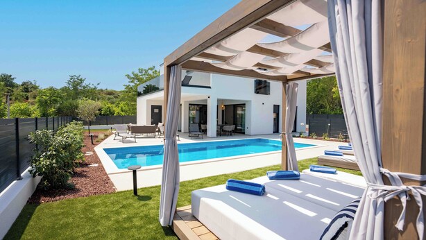 A modern outdoor pool area with a covered seating area and a bed with blue towels. - 5 stars Luxury Villa in Lopar on island Rab (LOPAR (RAB))