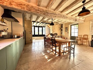 Una cocina amplia con una gran mesa de comedor, sillas de madera y techo rústico.