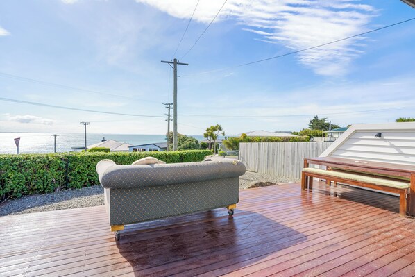 A wooden deck with a sofa and a bench, overlooking a body of water.