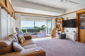 A living room with a brown leather sofa, a flat-screen TV, a bookshelf, and a view of the outdoors.