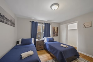 Une chambre avec deux lits, une fenêtre avec des rideaux, une table de chevet et une porte.
