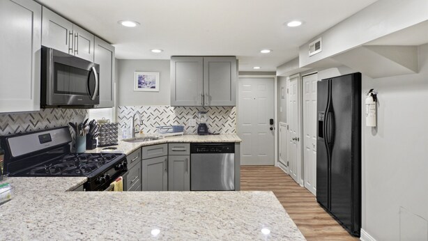 A modern kitchen with grey cabinets, a stainless steel microwave, a black refrigerator, and a dishwasher. - Quiet Area - Revamped Basement (Chicago)