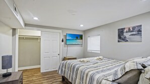 A bedroom with a bed, a TV, a painting, and a window with blinds. - Quiet Area - Revamped Basement (Chicago)