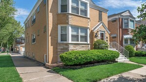 A two-story residential building with a brick facade, large windows, and a small front porch. - Quiet Area - Revamped Basement (Chicago)