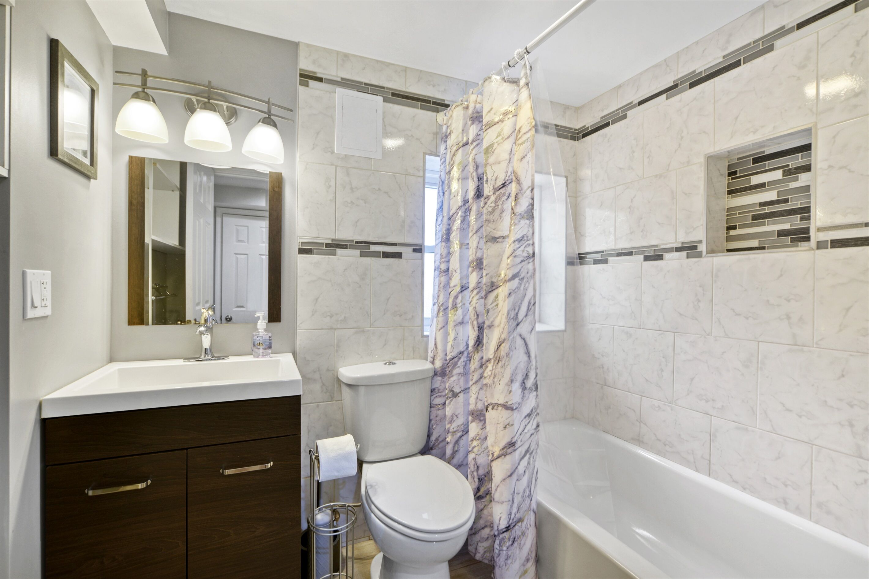 Une salle de bain avec un rideau de douche en marbre, des toilettes blanches, un lavabo avec un miroir et une baignoire.