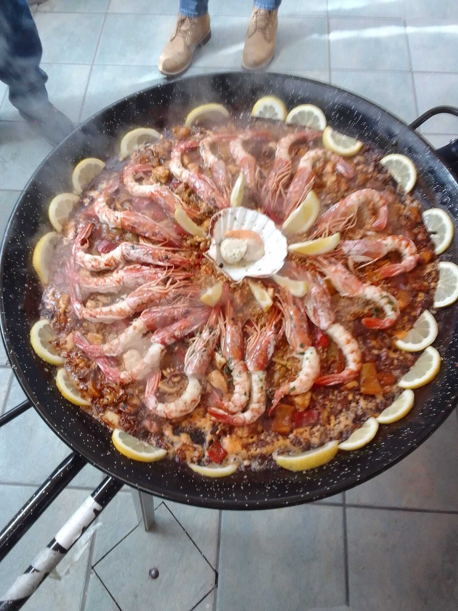 Una paella de mariscos generosa, con camarones y rodajas de limón, servida en una sartén negra.