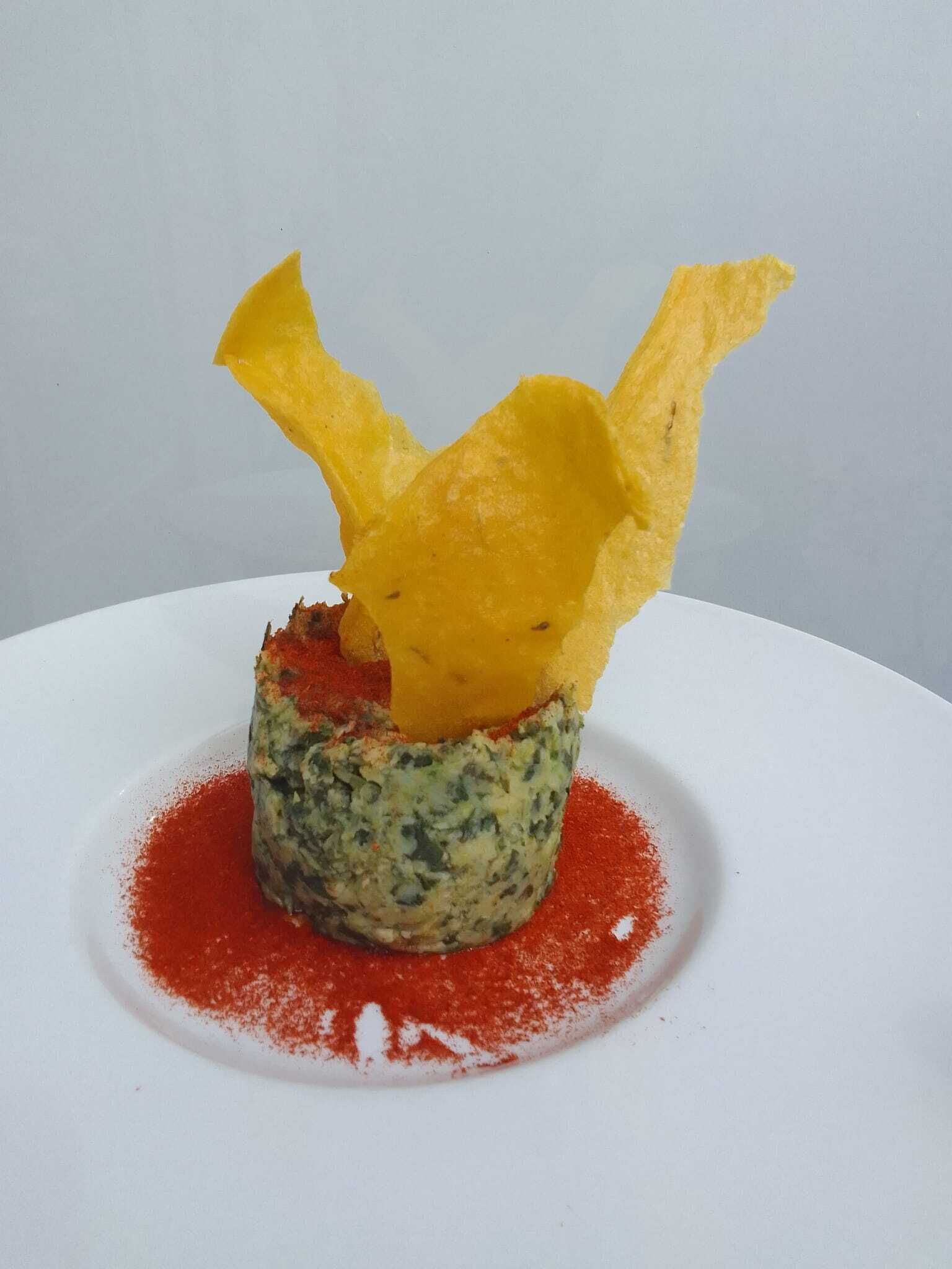 Un plato con un elemento amarillo y crujiente encima, una base verde y salsa roja alrededor.