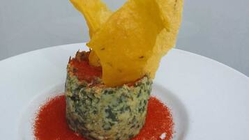 Un plato con un elemento amarillo y crujiente encima, una base verde y salsa roja alrededor.