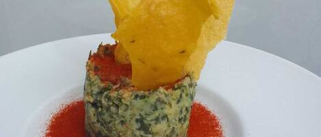 A dish with a yellow, crispy element on top, a green base, and red sauce around it.