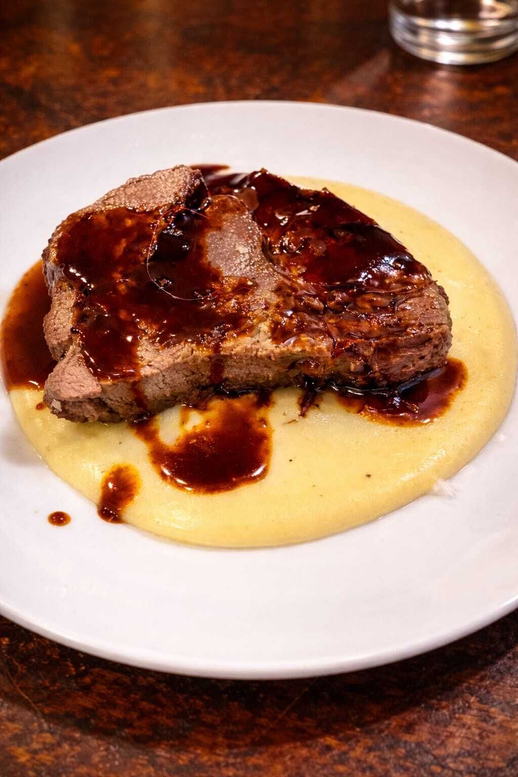 A steak with a dark sauce on a white plate.