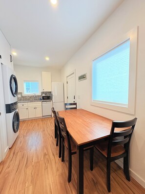 A compact kitchen with a wooden dining table and chairs, a washing machine, and a refrigerator.