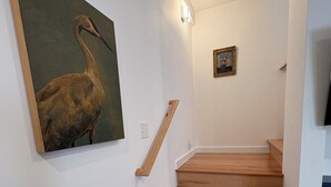 Uma escadaria com degraus de madeira e corrimão, um quadro de um pássaro na parede e uma pequena moldura na parede.