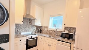 Uma cozinha moderna com armários brancos, bancadas de granito, forno embutido, micro-ondas e lava-louças.