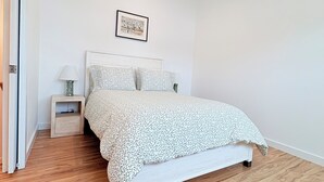 Quarto com cama, mesa de cabeceira, quadro emoldurado na parede e piso de madeira.