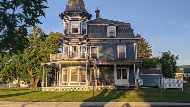 Ein im viktorianischen Stil gehaltenes Haus mit einem markanten Turm, einer umlaufenden Veranda und einem gepflegten Rasen.