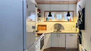Ett kompakt kök med vita skåp, en inbyggd ugn, en diskho och ett fönster ovanför bänkskivan.