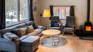 Ett mysigt vardagsrum med en grå soffa, två fåtöljer, ett runt soffbord och en vedeldad kamin.