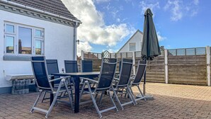 A patio with a table and chairs, a wooden fence, and a house with a tiled roof. - Cozy home in Hanstholm with WiFi (Hanstholm)