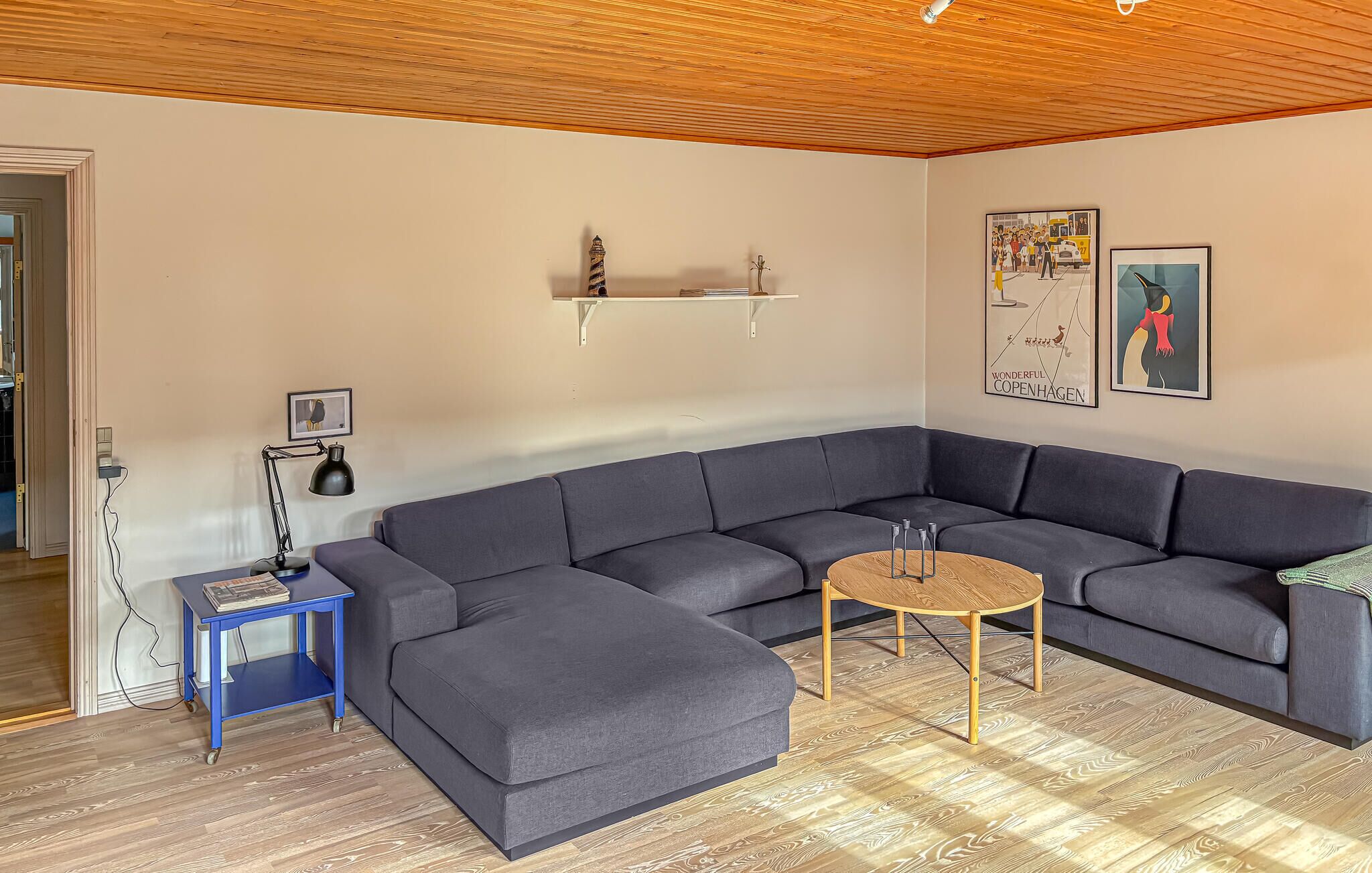 A living room with a sectional sofa, a small round coffee table, and a lamp on a blue side table.