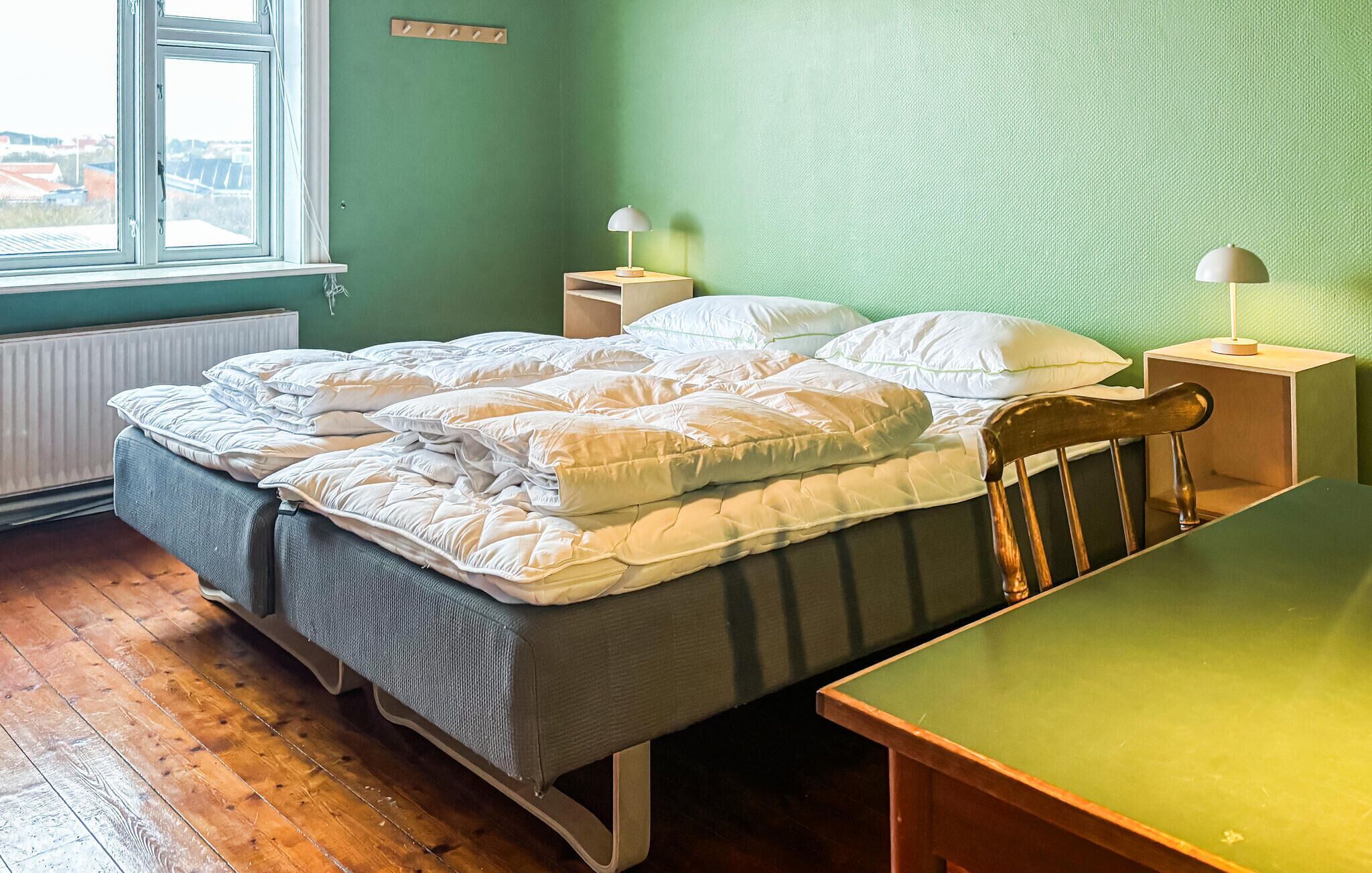 A single bed with a wooden headboard, a bedside table with a lamp, and a view of the outside through a window.