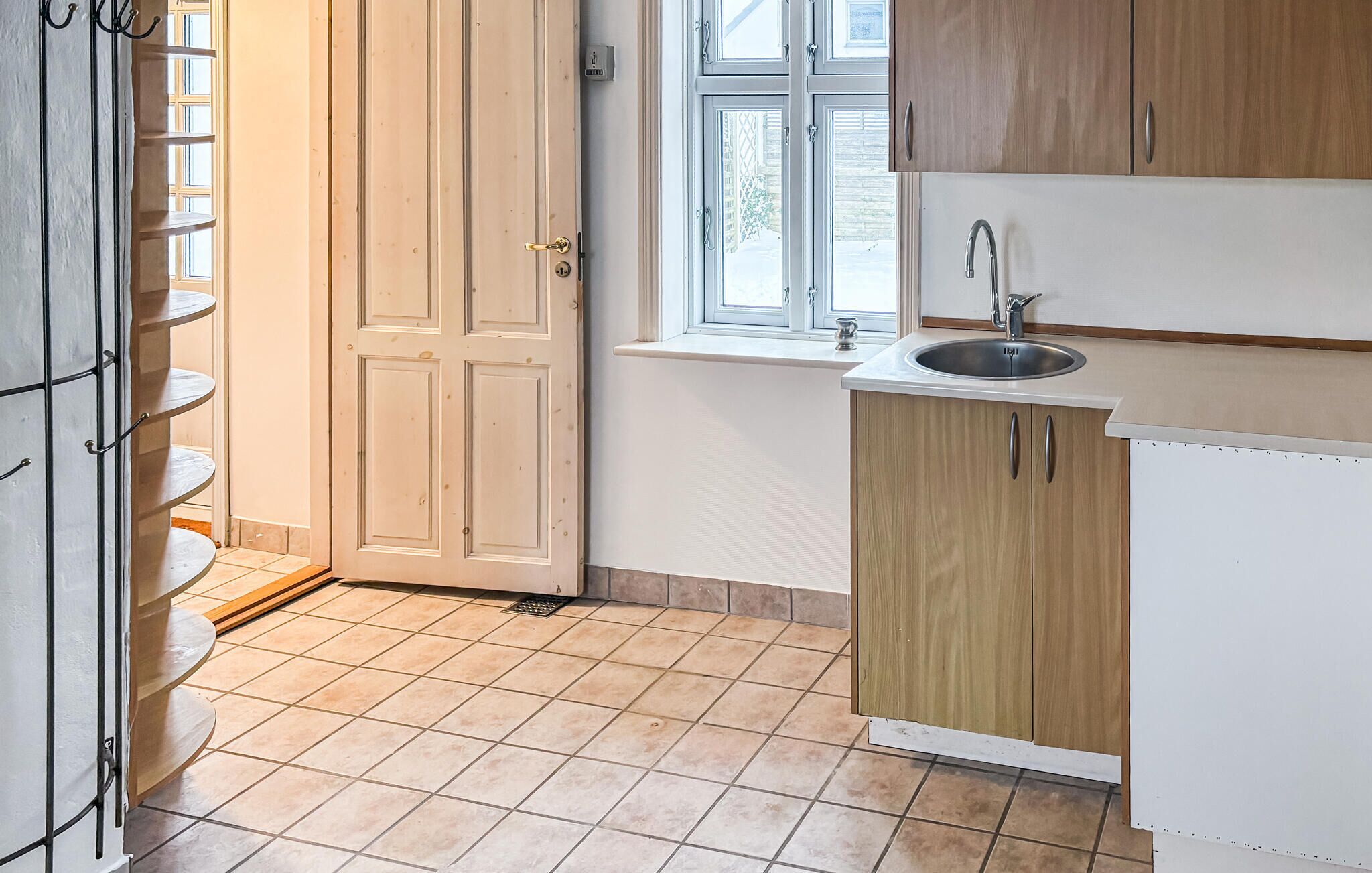 Una cocina con ventana, pileta y puerta.