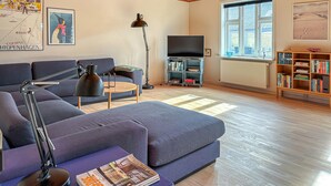 A modern living room with a sofa, a coffee table, a floor lamp, a TV stand, and a bookshelf. - Cozy home in Hanstholm with WiFi (Hanstholm)