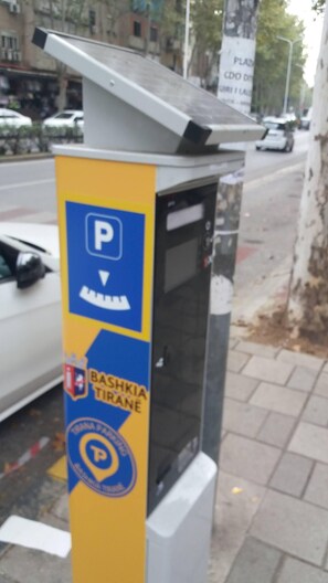 A parking meter with a blue and yellow sign indicating a parking area. - Apartment near markets and local vibrant vibe (Tiranë)