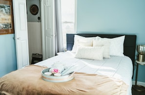 Ein Schlafzimmer mit einem Bett, Kissen, einer Ablage mit Blumen und einem Fenster.