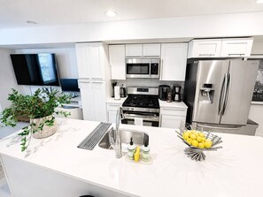 Cocina moderna con armarios blancos, electrodomésticos de acero inoxidable y una isla central con lavamanos y un cuenco de limones.