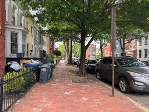 A brick-paved sidewalk with parked cars and trash bins on the side. - Stylish Work-Friendly 2BR | Shaw Metro & Dining (Washington)