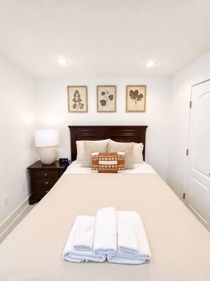 A neatly made bed with a headboard, a bedside lamp, and a clock on the nightstand. - Stylish Work-Friendly 2BR | Shaw Metro & Dining (Washington)