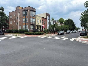 A multi-story building with a stop sign at the corner, a crosswalk, and parked cars. - Stylish Work-Friendly 2BR | Shaw Metro & Dining (Washington)