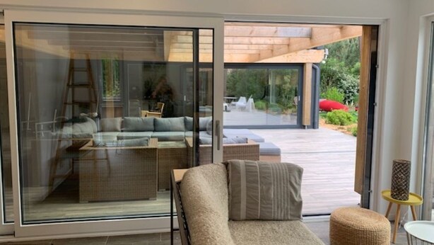 Un salon moderne avec un canapé, une porte coulissante en verre donnant sur une terrasse extérieure et une petite table ronde.