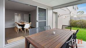 Un comedor con una mesa y sillas de madera, una puerta corrediza de vidrio que da a una cocina y vistas a un patio trasero con un tendedero.