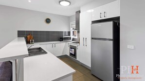Una cocina moderna con armarios blancos, un refrigerador de acero inoxidable, un microondas y un horno empotrado.