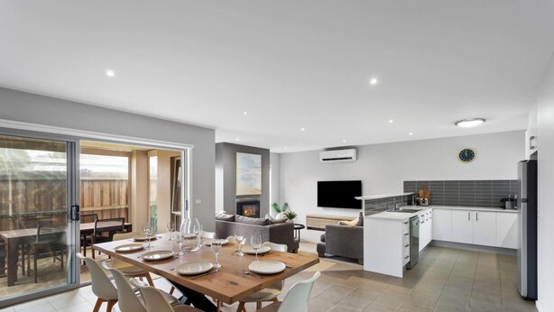 Una cocina moderna con estufa integrada, un comedor con mesa de madera dispuesta para cuatro personas, y un amplio ventanal corredero que da a un patio exterior.