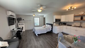 Un espacio habitable compacto con cama, escritorio con ordenador, kitchenette y zona de comedor con mesa de vidrio.