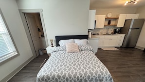 Un dormitorio con cama, mesita de noche, cómoda y kitchenette.