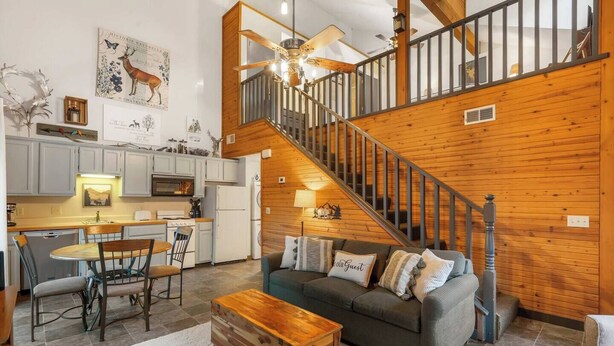 A spacious living area with a wooden staircase, a dining table, and a cozy sofa. - Adorable 2-bedroom condo cabin with AC in lively Branson close to everything! (Branson)