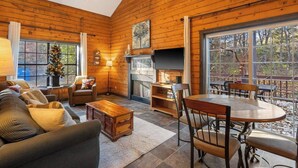 A cozy cabin interior with a fireplace, wooden walls, a dining area, and large windows. - Adorable 2-bedroom condo cabin with AC in lively Branson close to everything! (Branson)
