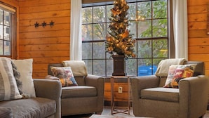 A cozy room with two grey armchairs, a small wooden table, and a Christmas tree. - Adorable 2-bedroom condo cabin with AC in lively Branson close to everything! (Branson)