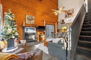 A cozy log cabin interior with a fireplace, a Christmas tree, a dining area, and a staircase. - Adorable 2-bedroom condo cabin with AC in lively Branson close to everything! (Branson)