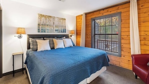 A bedroom with a large bed, wooden walls, a window with a view, and a red chair. - Adorable 2-bedroom condo cabin with AC in lively Branson close to everything! (Branson)