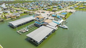 An aerial view of a marina with docks, a boat, and a building with a blue roof. - Teal Turtle - Sassy & Sophisticated Sea Isle Spot (Galveston)
