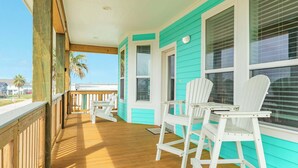 A covered porch with wooden flooring, white Adirondack chairs, and turquoise walls. - Teal Turtle - Sassy & Sophisticated Sea Isle Spot (Galveston)