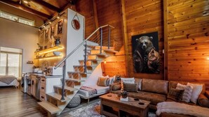 Een gezellig interieur van een chalet met een houten trap, een bank, een salontafel en een beren schilderij aan de muur.
