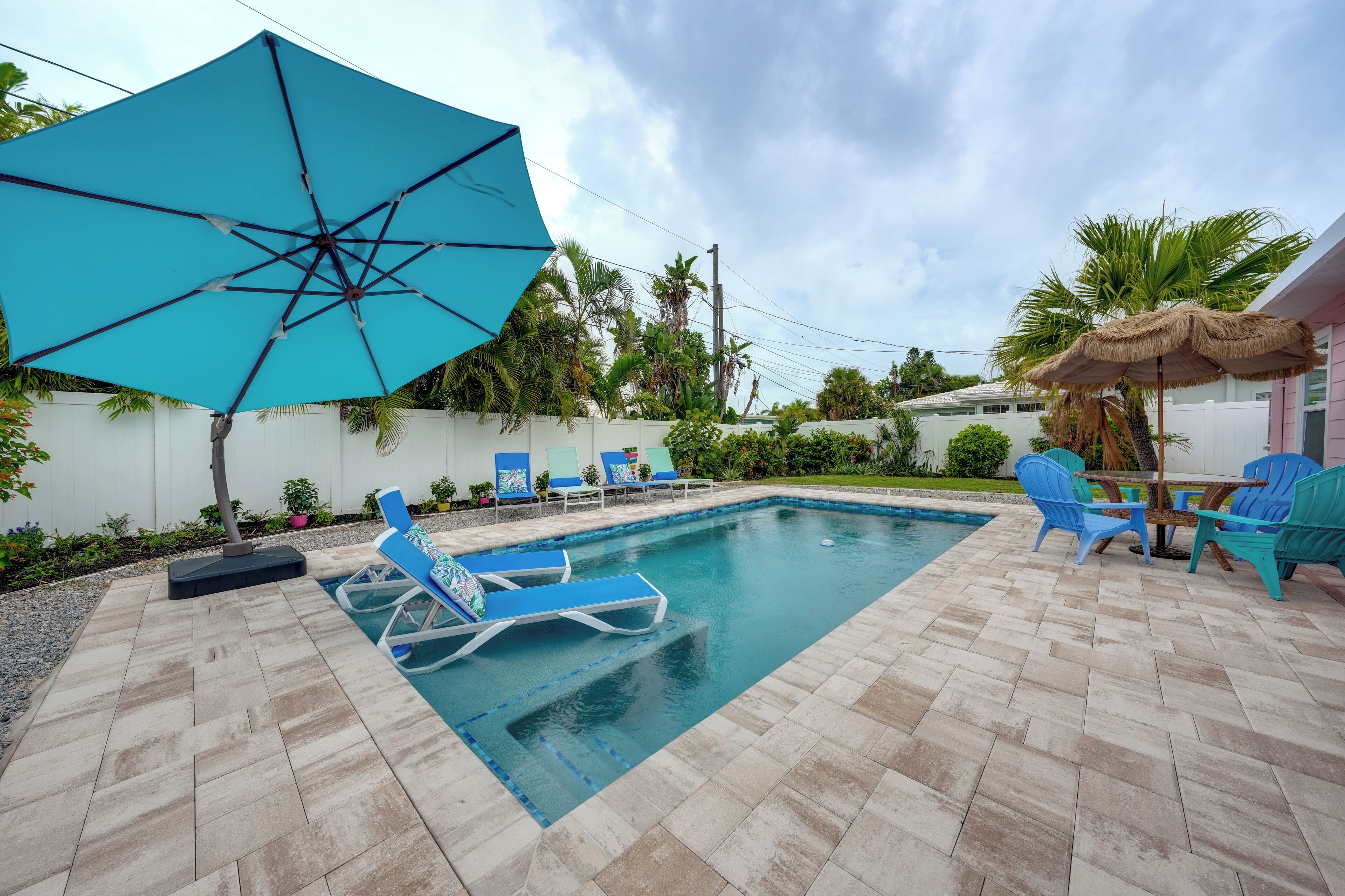 A swimming pool with blue lounge chairs and an umbrella.